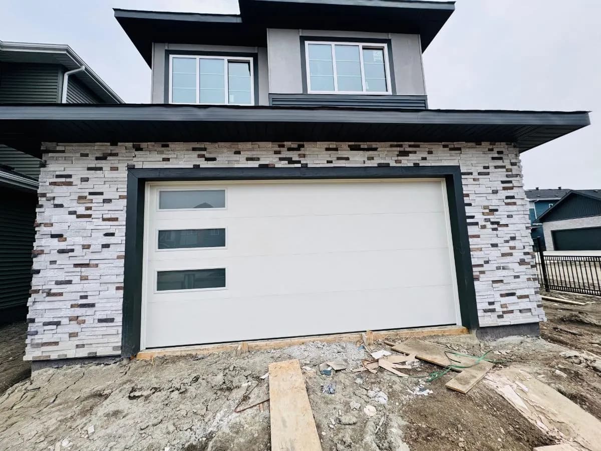 A white flush garage door on a stone-clad new build, installed by Eagle Garage Doors